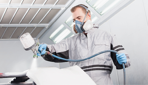 Mann lackiert Autoteil mit Sprühpistole in Lackierkabine.